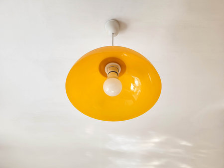 A round yellow glass lampshade with a white lamp hangs under a white ceiling