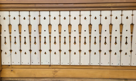 Flat white balusters on the wooden wall. Carved wooden board fence