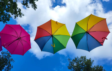 Colorful beautiful umbrellas under the blue sky hanging over the alley of the city park.の写真素材