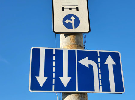 White arrows on a blue background are a standard road sign on a vertical pole against the sky.の写真素材