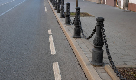 Black wrought iron poles with chains, fences by the road. An old fence.
