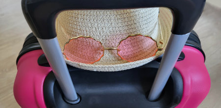 There is a baby hat and sunglasses on a pink children's suitcase with a handleの写真素材