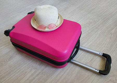 A child's hat and pink glasses are lying on a pink children's suitcase. The concept of children's recreation.の写真素材