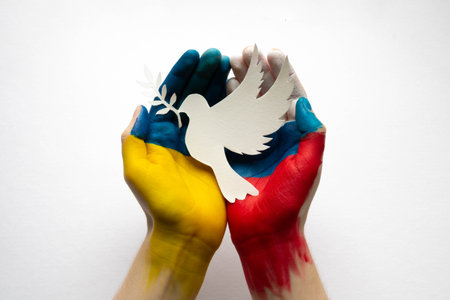 Human hands decorated with flags of Russia and Ukraine stand out against a white background, holding a paper pigeon together. The concept of peace, friendship and creation.の写真素材