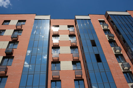 The reflection on the glass facade of the house shows a blue sky with white clouds