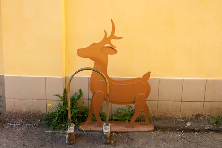 A small brown deer is standing outside in front of a house wall.の写真素材