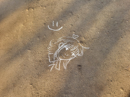 A girl with a smile is drawn on gray asphalt with white chalkの写真素材