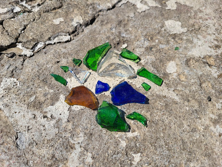 Shards of green, blue, white, and brown glass lie on the concreteの写真素材