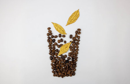 A glass with golden leaves falling into it is lined with coffee beans on a white background. The concept of harvesting.の写真素材