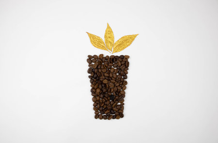 Golden leaves above a glass lined with coffee beans on a white background. Harvesting conceptの写真素材