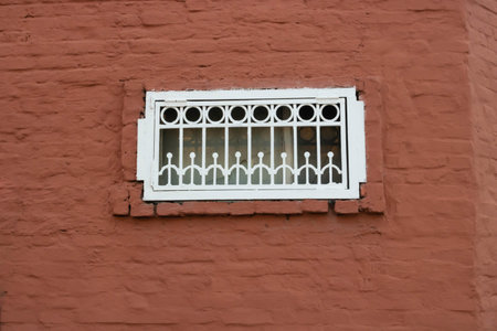On a dark red brick wall, a small window with a white grille.