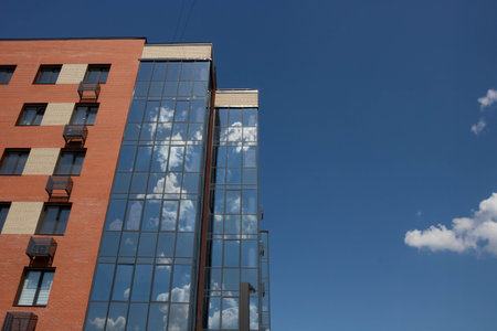 The facade of a red building with large windows on a blue sky background with reflections of white...