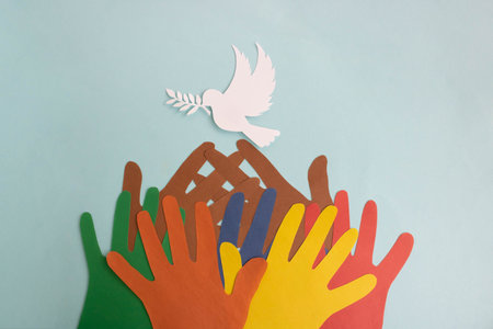 Colored paper hands reach out to a paper dove of peace on a blue background. World Peace Dayの写真素材