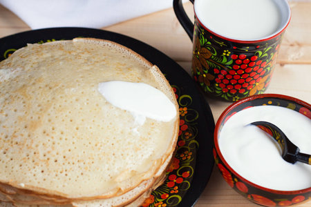 Pancakes with sour cream and milk in the Russian utensils made of wood with paintingの写真素材