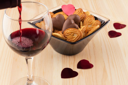 Red wine is poured into a glass, next vase with cookies and chocolates in the form of heartsの写真素材