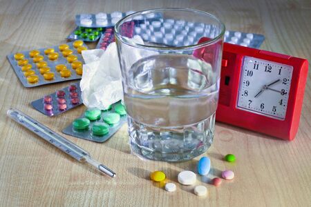 Medicines tablets, pills and water in a glass on the table with alarm clockの写真素材