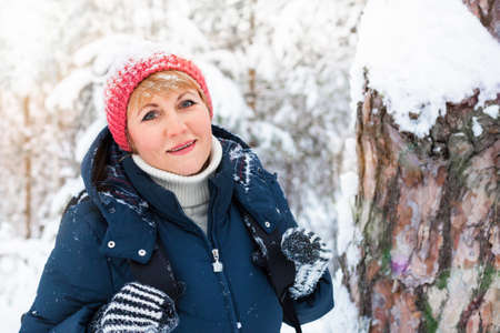 Happy woman walking in winter forest. A middle-aged woman is freezing in the Park. Beautiful Sunny weather. She smiles.の写真素材