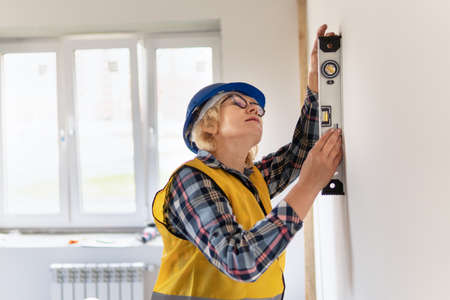 Female construction worker with level. A middle-aged woman in a helmet checks the quality of repairs.の写真素材