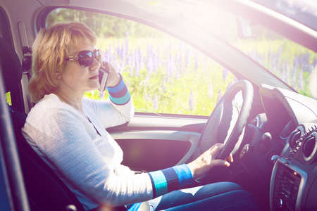 A woman driving a car. Mature middle-aged woman rides in a car in the summer in nature.