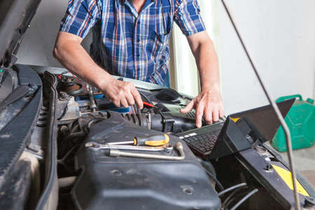 The hand of a car repairman with a laptop. Car repair in an auto repair shop.の写真素材