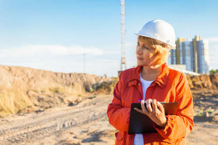 A female construction engineer is at a construction site. The woman inspects.