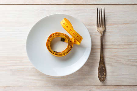 There is a fork and measuring tape on the saucer. The concept of a healthy lifestyleの写真素材