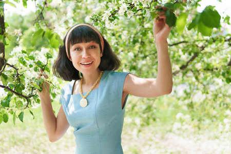 A beautiful woman in a blue dress under a flowering tree in the garden in spring. The brunette...