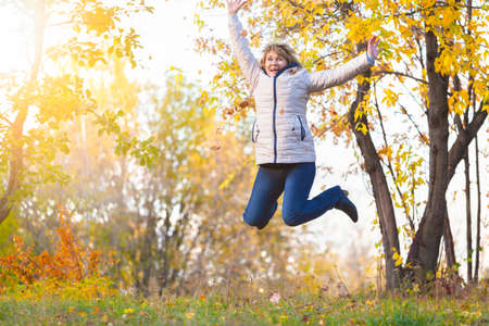 Cute middle-aged woman in nature in autumn. Mature woman walking in the park, she is happy. She...