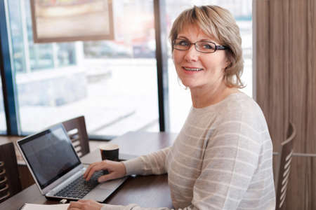 A woman is engaged in business at the workplace in a cafe, office. A middle-aged woman is working on...