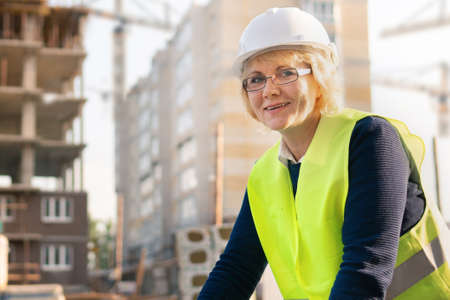 A female construction worker in a vest and helmet on the background of a new building. She smiles.の写真素材