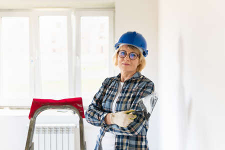 Female construction worker with a construction tool. A middle-aged woman in a hard hat makes repairs in the apartment.の写真素材