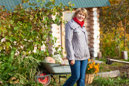 A woman with a basket is in the garden. A middle-aged woman in jeans and a jacket holds flowers...