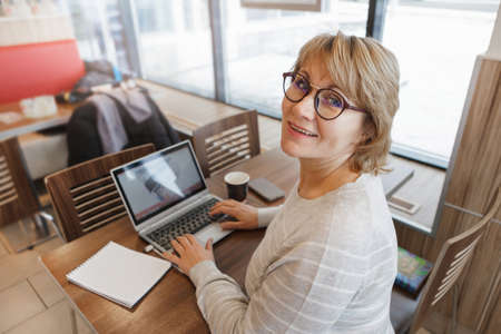 A woman in a cafe is working on a laptop. She smiles. A middle-aged woman, an adult in an office....