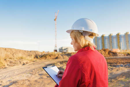 A female construction worker is on a construction site. A middle-aged woman in a white helmet with a...