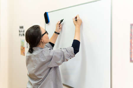 A woman leads a lesson at the marker Board. A middle-aged woman leads a business training session with a marker in her hand.の写真素材