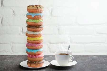 Sweet colored donuts and hot cup of coffee on a table near a white brick wall. Breakfast concept.の写真素材