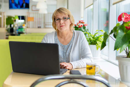A woman with a laptop is working in an office. A middle-aged woman is a businesswoman in a cafe. It...