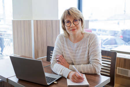 A woman does business in a cafe. A middle-aged woman works on her laptop in the office at the...