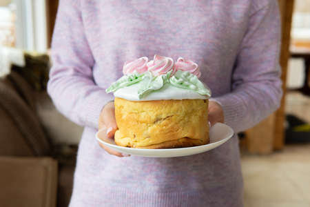 A woman holds a traditional Easter cake on the table.