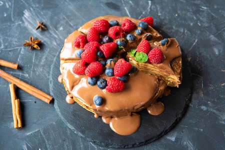 Pancakes with dessert filling and berries on a dark background.