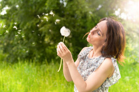 Girl blows a dandelion in nature and walks in parkの写真素材