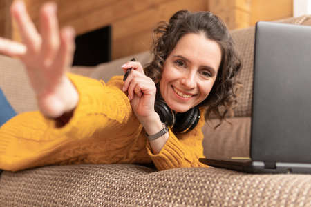 A woman works with a laptop and sits on a sofa in the house
