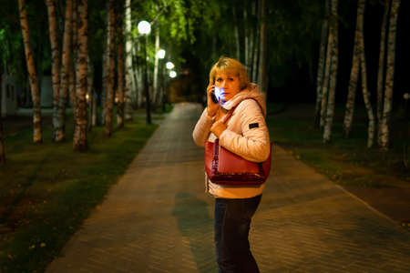 A woman with a mobile phone in her hand is walking through the night city.