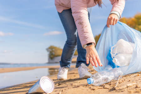 A female volunteer cleans plastic garbage in nature. It is located on the river bank with a waste bag. The concept of ecology.の写真素材