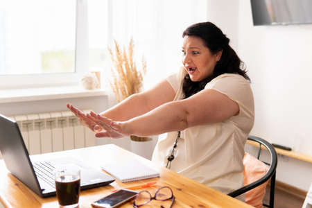 A woman is sitting in a room at a table with a laptop.