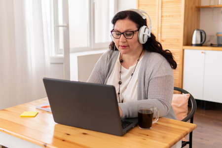 A fat woman is sitting at a table with a laptop.