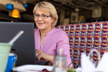 A woman sitting at a table with a Cup of tea and a laptop working in a cafe.