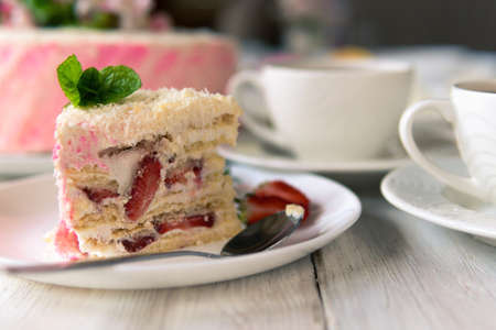A piece of baked cake with berries and cream on a plate on a white wooden background