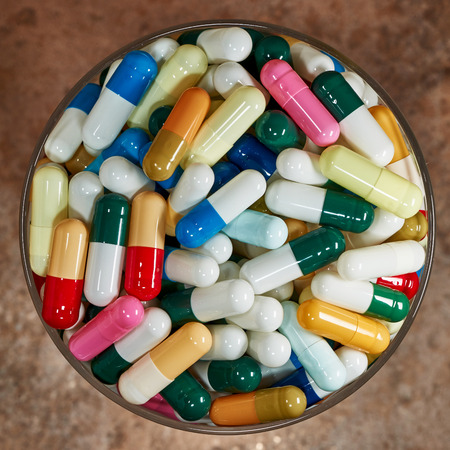 Medicinal capsules of many colors photographed from above in a glass