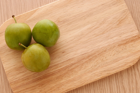 Three green plums placed on a wooden cutting boardの写真素材